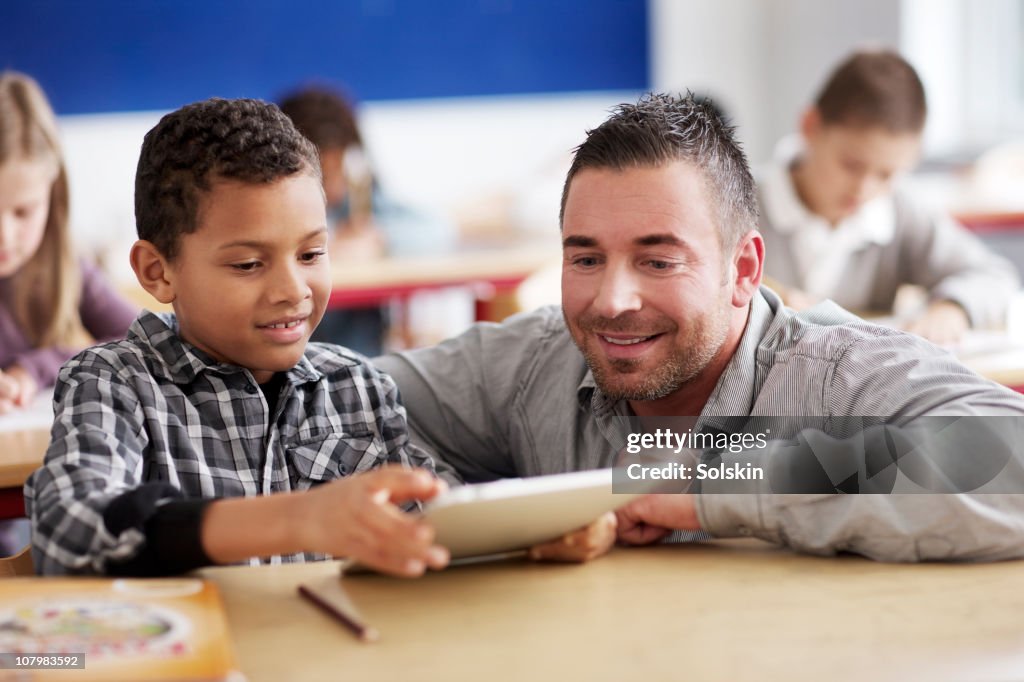 Boy showing teacher schoolwork on tablet computer