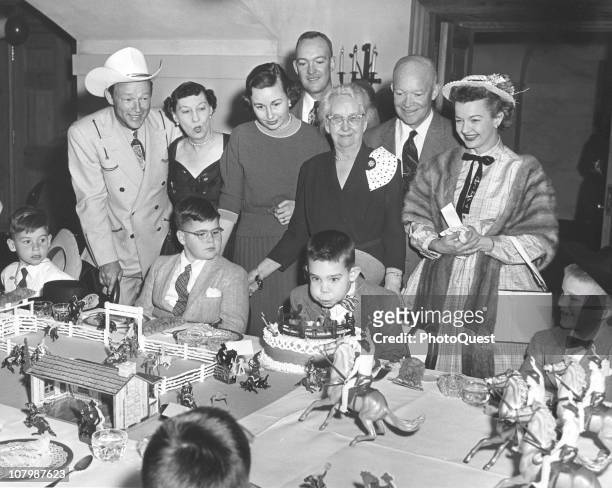 David Eisenhower blows out the candles on his birthday cake at a cowboy-themed party in the White House, Washington DC, March 31, 1956. Among the...