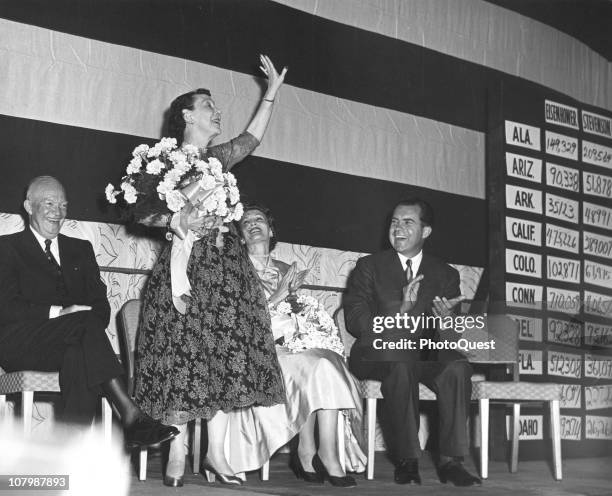 American First Lady Mamie Eisenhower holds a bouquet of flowers as she waves from a stage as presidential election rsults are tallied; behind her is...