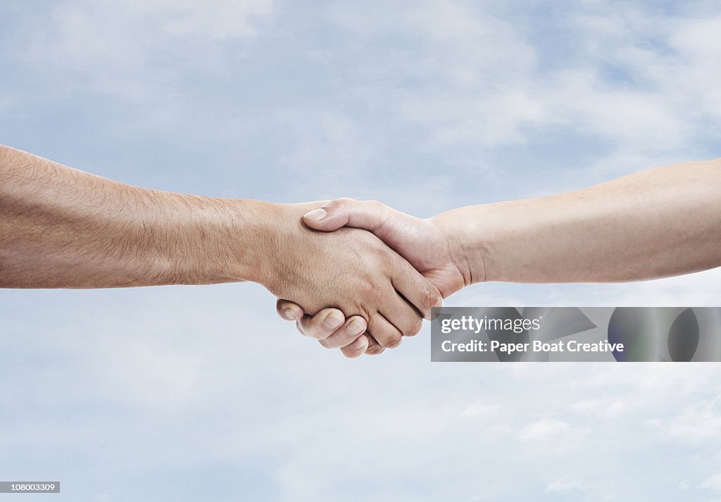 Two men shaking hands againt sky background