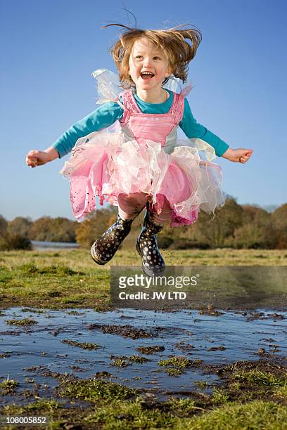 girl in fancy dress costume jumping in muddy puddle - girls misbehaving stock pictures, royalty-free photos & images