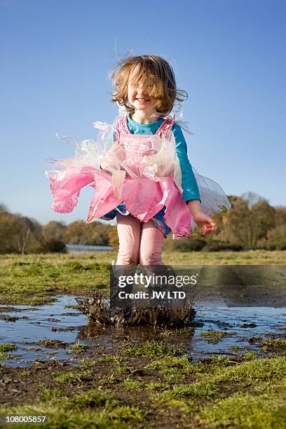 girl in fancy dress costume jumping in muddy puddle - mädchen kleid stock-fotos und bilder