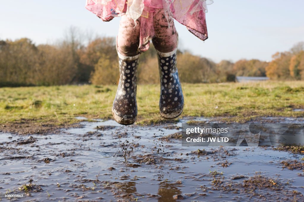 Girl wearing wellington boots jumping in muddy puddle