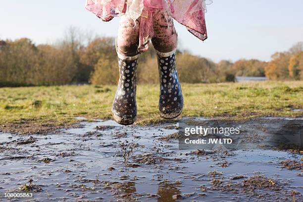 girl wearing wellington boots jumping in muddy puddle - puddles stock-fotos und bilder