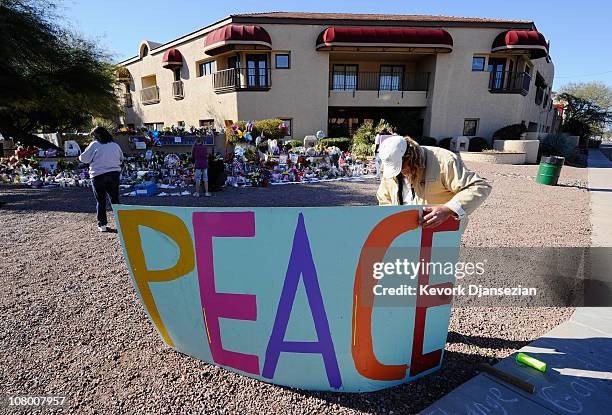 Troy Wine places a large peace sign at a makeshift memorial outside the office of Rep. Gabrielle Giffords on January 12, 2011 in Tucson, Arizona....