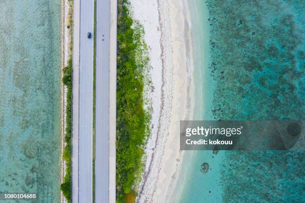 luftaufnahme von der fahrbahn auf beiden seiten vom meer umgeben - okinawa blue sky beach landscape stock-fotos und bilder