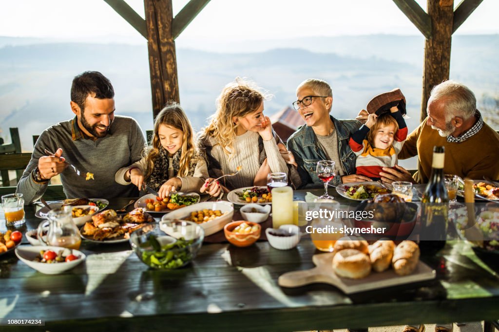 Happy extended family talking during lunch on a terrace.