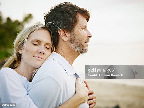wife embracing husband on beach at sunset - 40s couple stockfoto's en -beelden