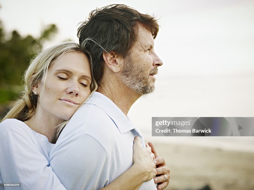 Wife embracing husband on beach at sunset