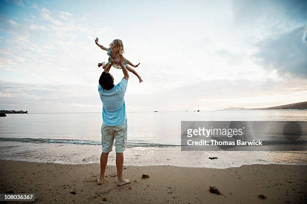 father lifting daughter overhead at sunset - retrieving foto e immagini stock