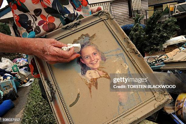 Narelle Cole gently wipes the fetid silt from a 21-year-old photo of her daughter Kerrie which she salvaged from the ruins of her inundated home in...