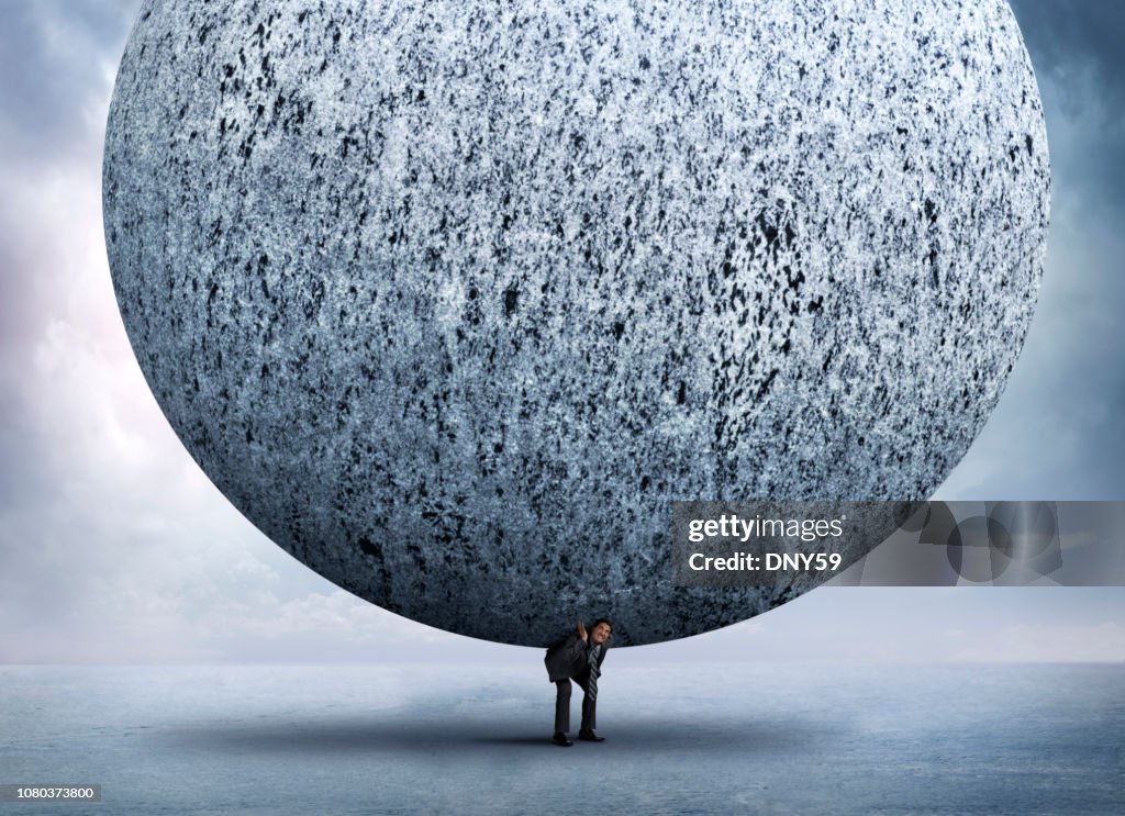 Businessman Bending Over To Support Very Large Stone Sphere On His Back