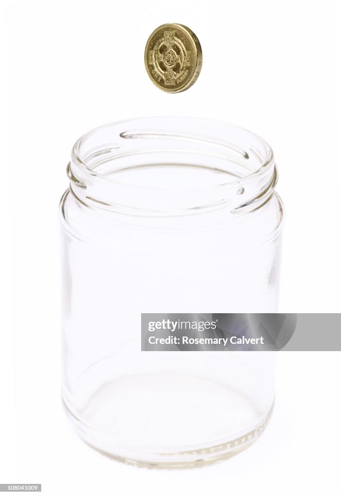 Empty jam jar with one pound coin falling into it.