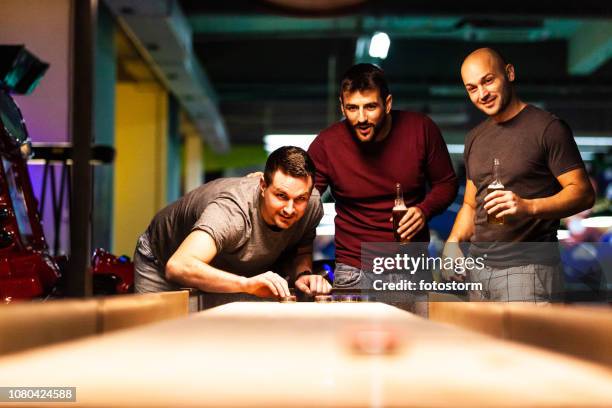 friends playing shuffleboard in pool hall - shuffle board table stock pictures, royalty-free photos & images