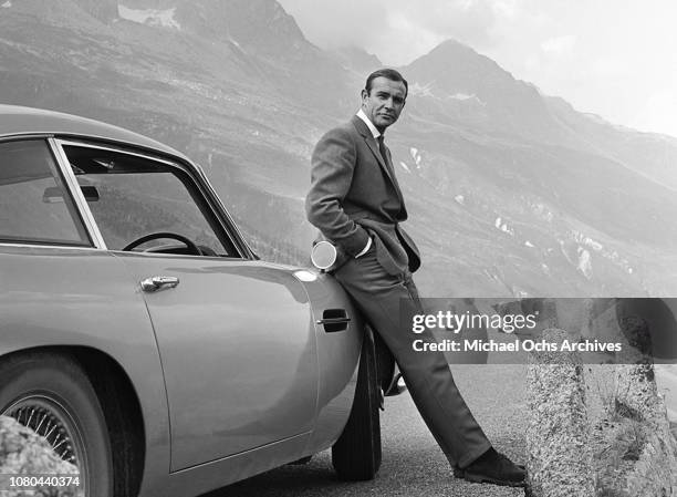 Actor Sean Connery poses as James Bond next to his Aston Martin DB5 during the filming of 'Goldfinger', Switzerland, 1964.