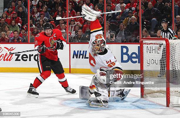 Henrik Karlsson of the Calgary Flames makes a blocker save as Daniel Alfredsson of the Ottawa Senators positions himself outside the crease at...