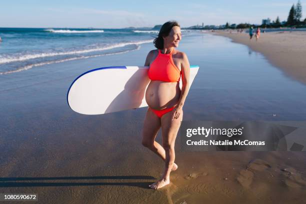 portrait mature pregnant woman with surf board at beach - mature woman in sun foto e immagini stock