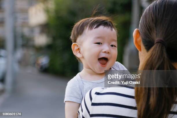 young mother holding baby boy in arms, relaxed and smiling on the road. - cute japanese boy stock-fotos und bilder