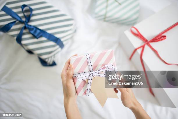female hand holding gift box with gift tag on the bed - gift lounge stock-fotos und bilder