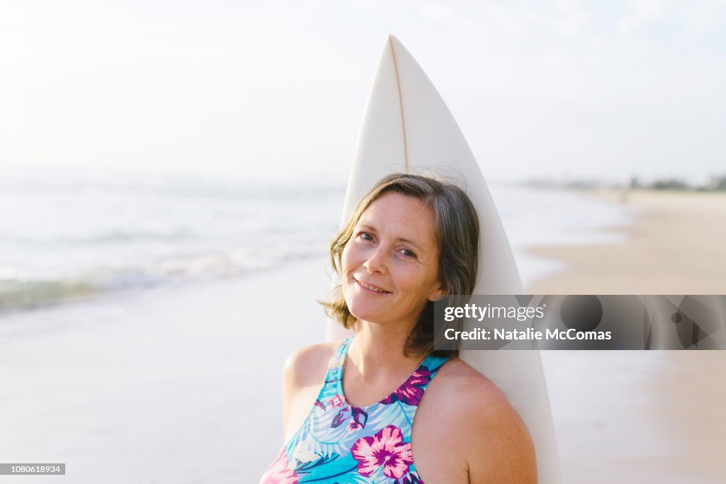 Portrait of mature woman on beach with surfboard