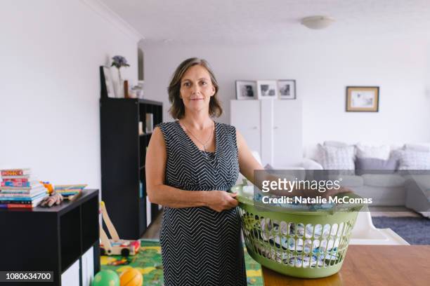 portrait of mature pregnant with laundry at home in living room - madre ama de casa fotografías e imágenes de stock
