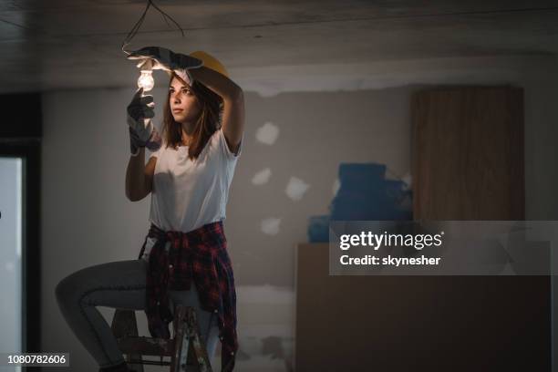 vrouwelijke elektricien aanscherping gloeilamp tijdens huisvernieuwing. - lampje-vervangen stockfoto's en -beelden