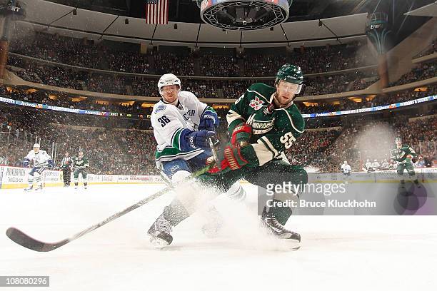 Nick Schultz of the Minnesota Wild and Jannik Hansen of the Vancouver Canucks skate to the puck during the game at Xcel Energy Center on January 16,...