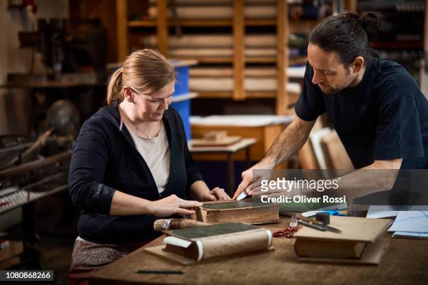 male and female bookbinder in workshop working on a book together - reliures photos et images de collection