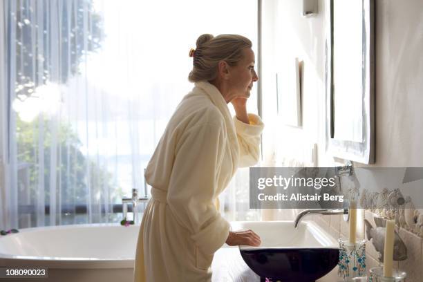 senior woman looking in bathroom mirror - female toilet stock pictures, royalty-free photos & images