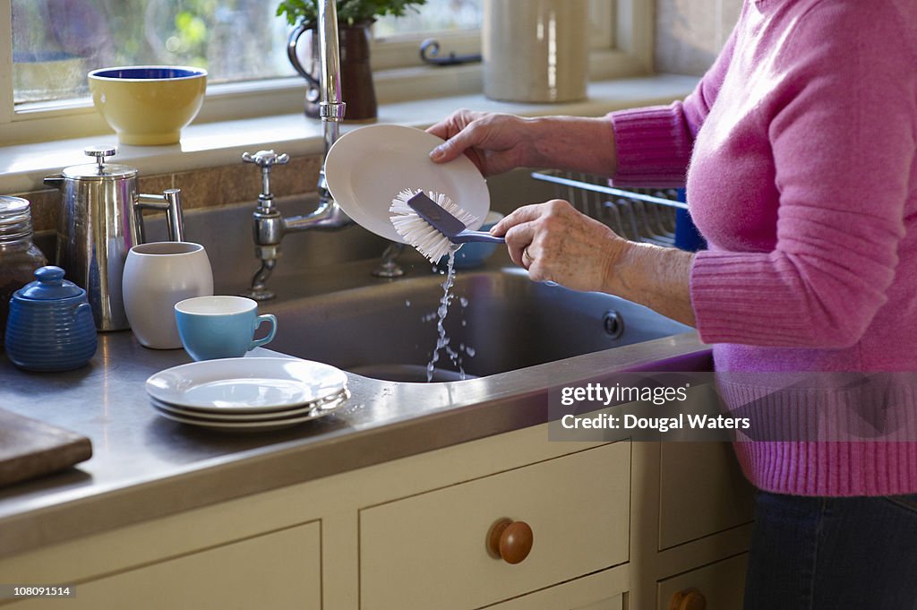 Woman washing up plates in sink.