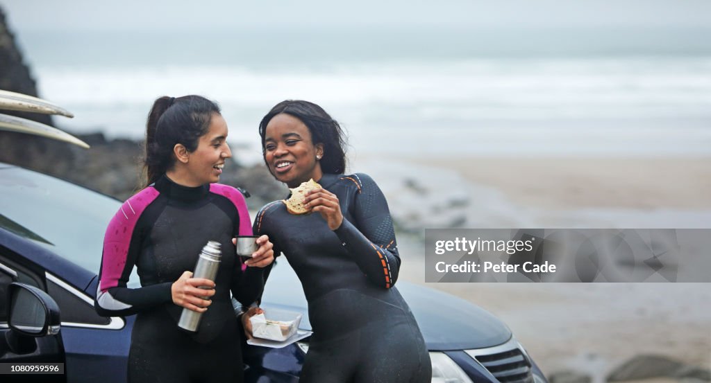 Two women having food by car after surfing