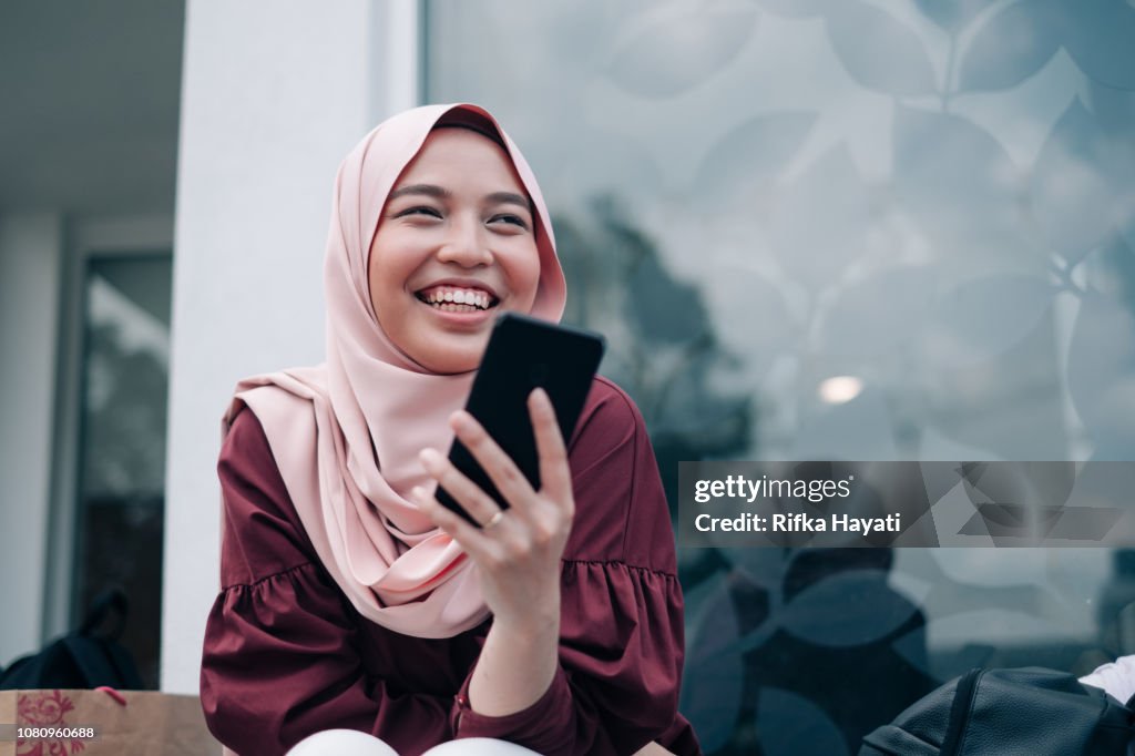 若いアジアのイスラム教徒の女性のスマート フォンを再生