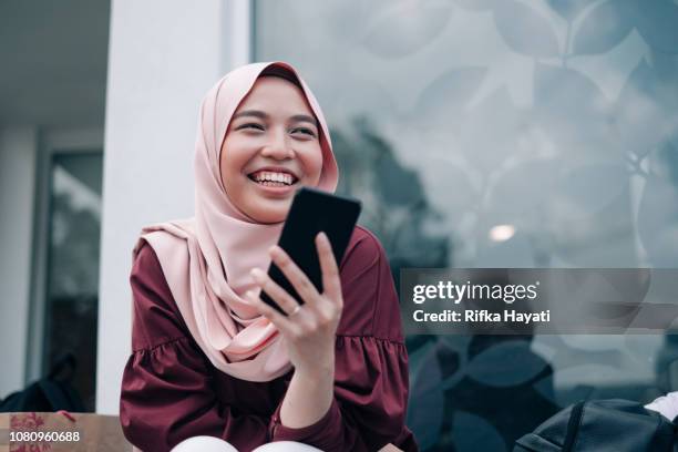 young asian muslim women playing smartphone - malaysian stock pictures, royalty-free photos & images