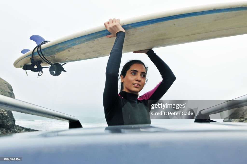 Young woman getting surfboard off car roof
