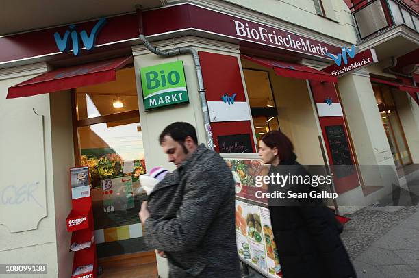 Couple with a young child walk past an organic grocery store in Prenzlauer Berg district on January 17, 2011 in Berlin, Germany. Gentrification in...