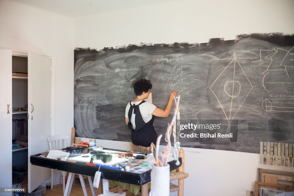 Young female artist drawing on a chalkboard in her studio