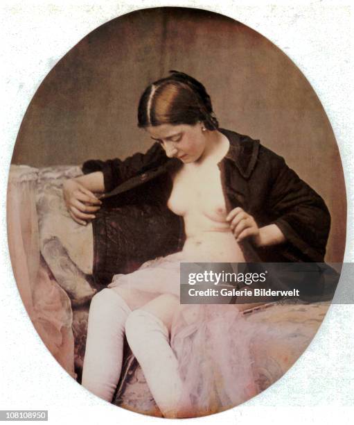 Woman is sitting on a chaise-longue wearing a blouse which she holds open exposing her breasts while a veil is covering her lap. 1850. Hand-colored...