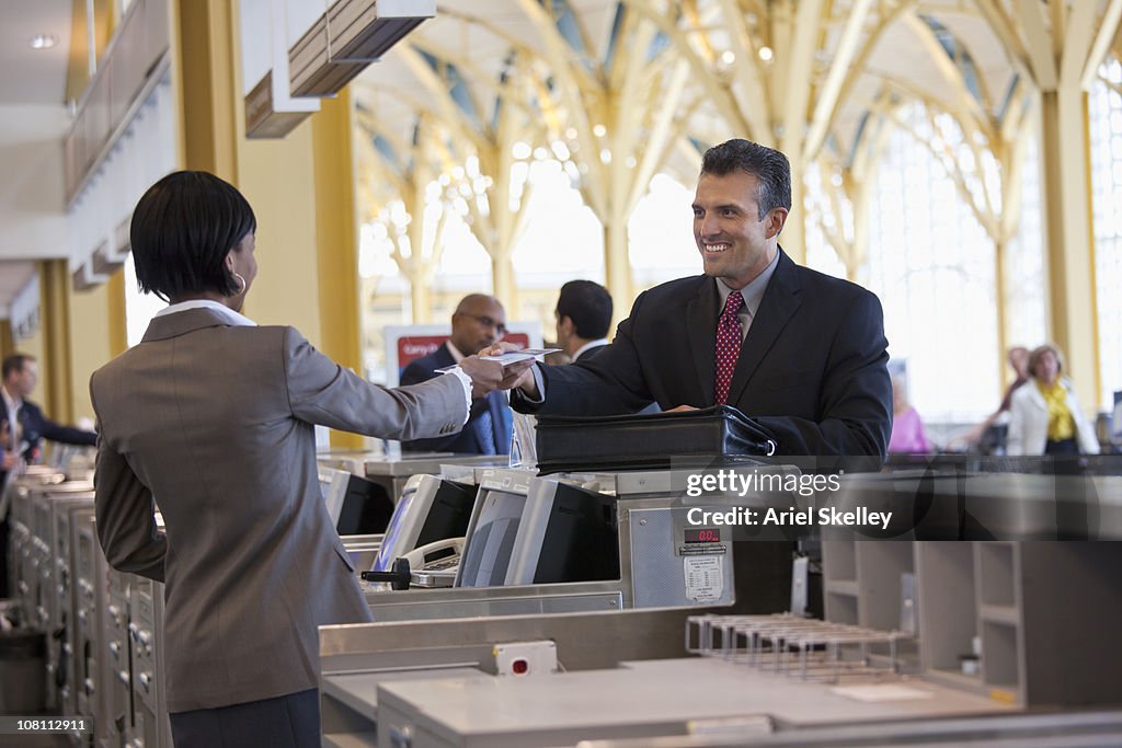 Clerk giving smiling businessman airplane ticket at airport counter