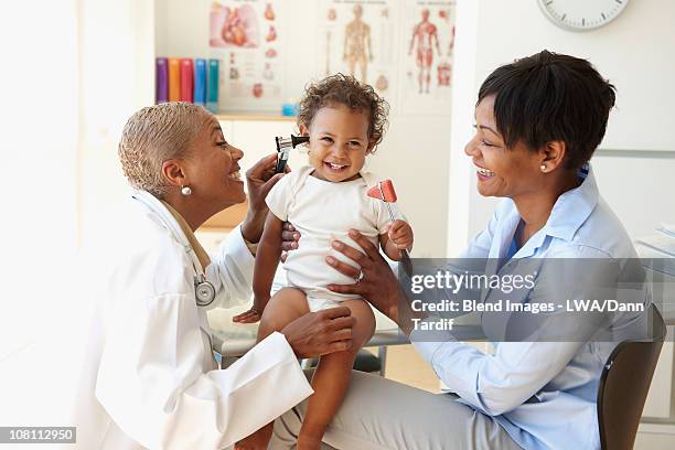 mother holding baby while doctor checks her ears - clinic canada diversity stock-fotos und bilder