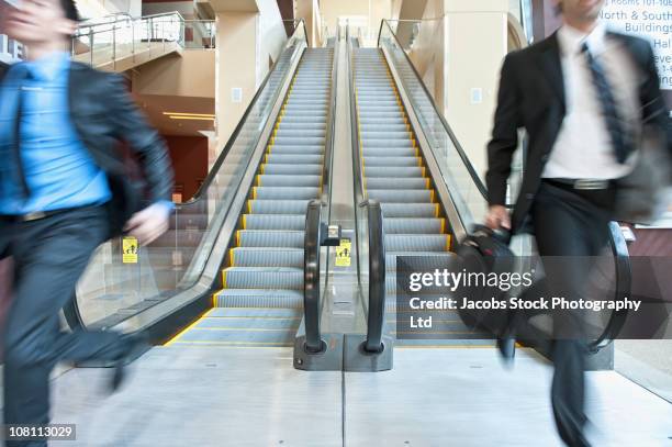 rushing businessmen running off escalator - running up an escalator stock pictures, royalty-free photos & images