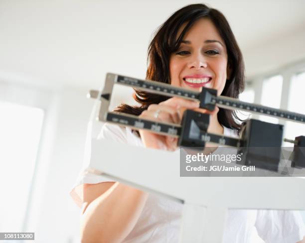 smiling hispanic woman weighing herself on scale - happiness scale stock pictures, royalty-free photos & images