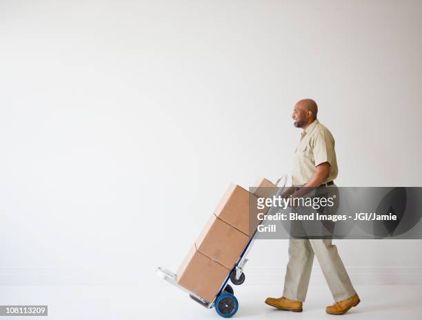 african american deliveryman pushing hand truck with boxes - sackkarre stock-fotos und bilder