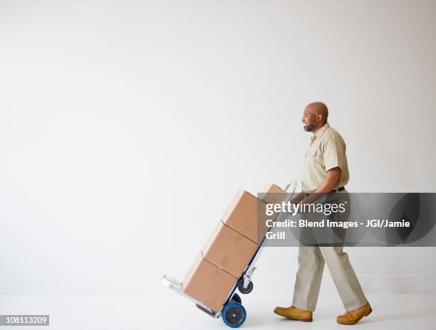 african american deliveryman pushing hand truck with boxes - delivery person on white stock pictures, royalty-free photos & images