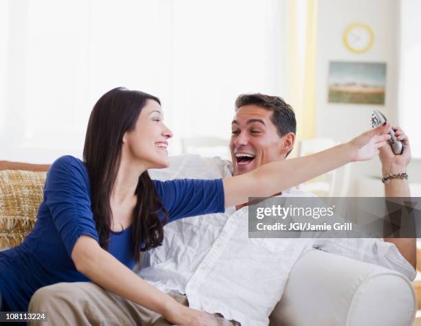 laughing mixed race man keeping remote control away from wife - teasing stock pictures, royalty-free photos & images