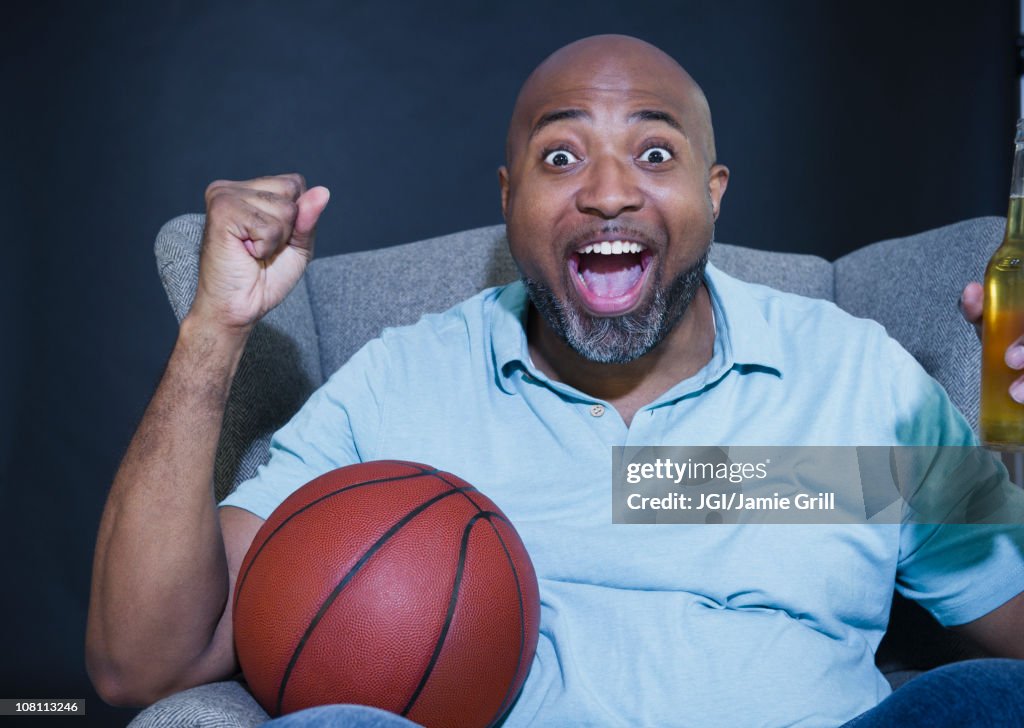 African American man drinking beer and watching basketball on television
