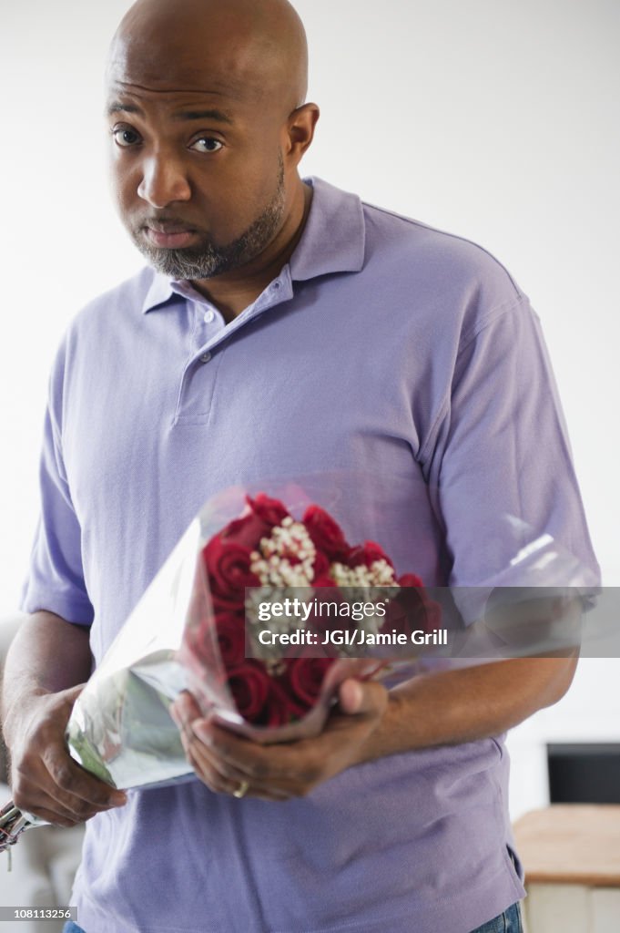 Sad African American man holding bouquet of roses