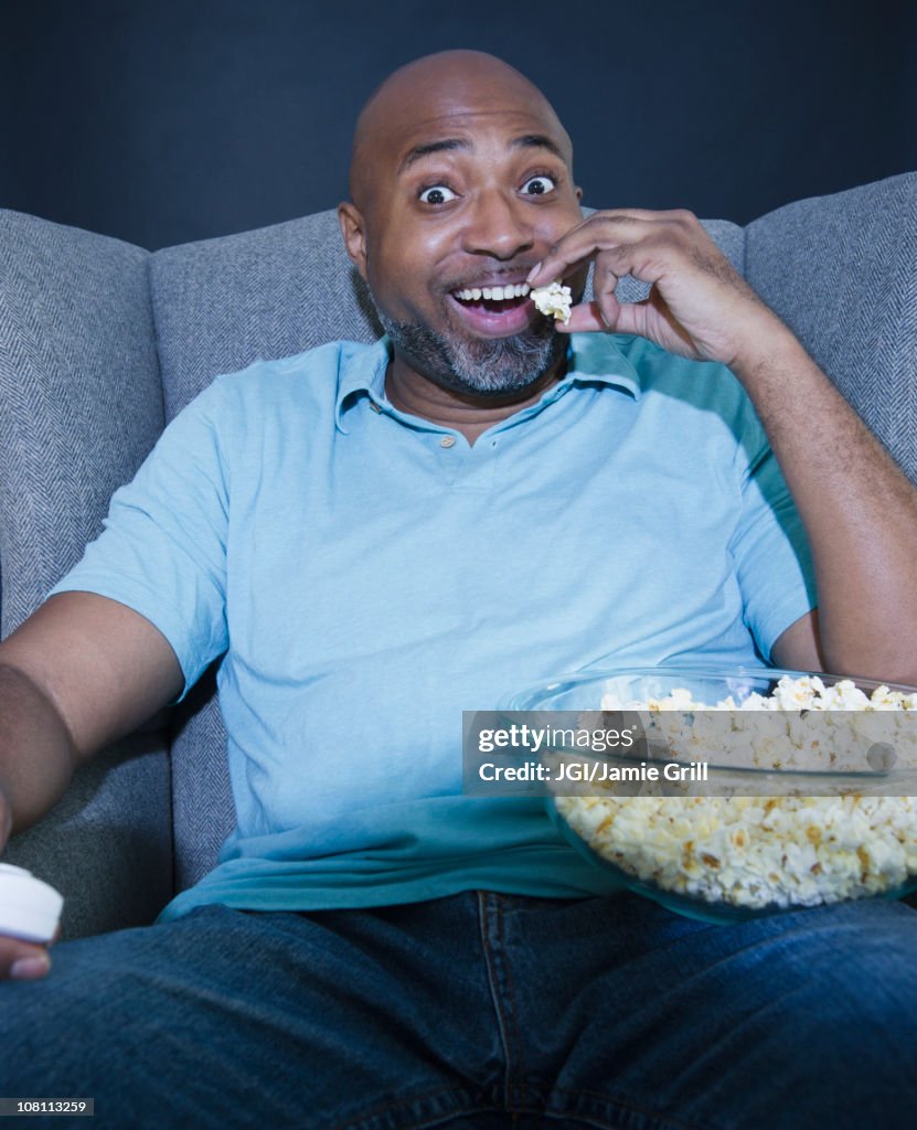 African American man eating popcorn and watching television