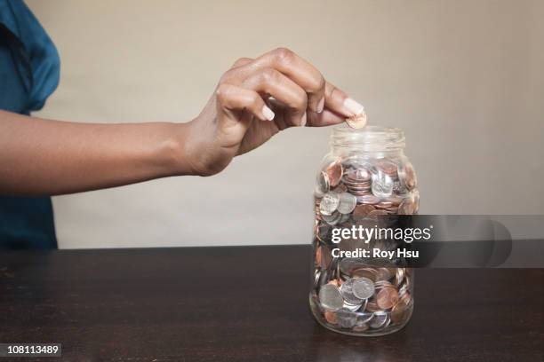black woman putting coin into jar - human hand positions stock pictures, royalty-free photos & images