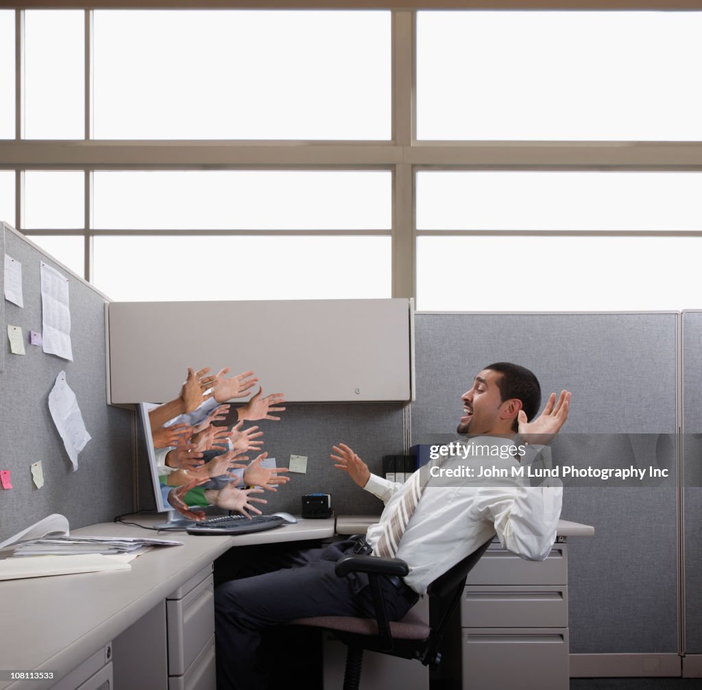 Hands reaching out from computer trying to grab Hispanic businessman