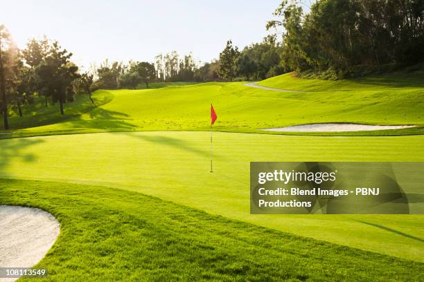 flag on golf course surrounded by sand traps - golfplatz-green stock-fotos und bilder